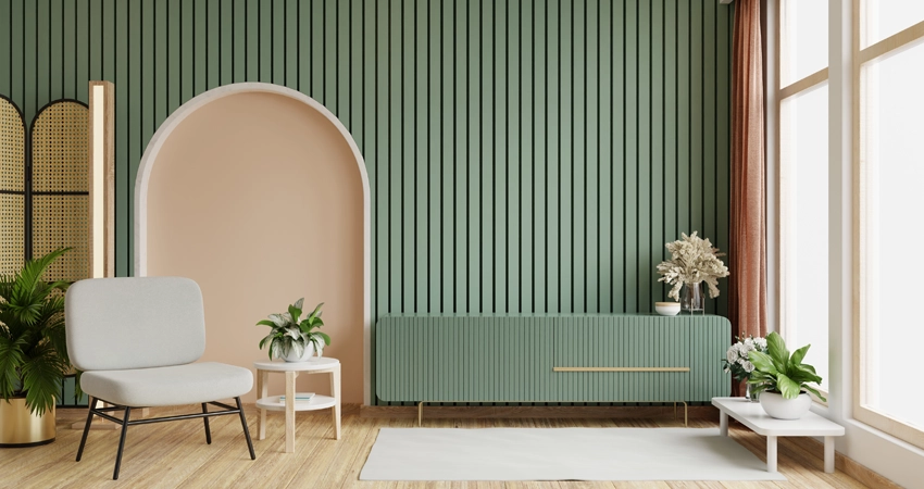 A modern living room featuring vertical wall paneling in a soft sage green color. The design includes an arched niche painted in a blush tone, complementing the muted palette. Furniture pieces include a minimalist chair, a sleek console table with gold accents, and a mix of greenery and floral arrangements, creating a cozy and sophisticated ambiance.