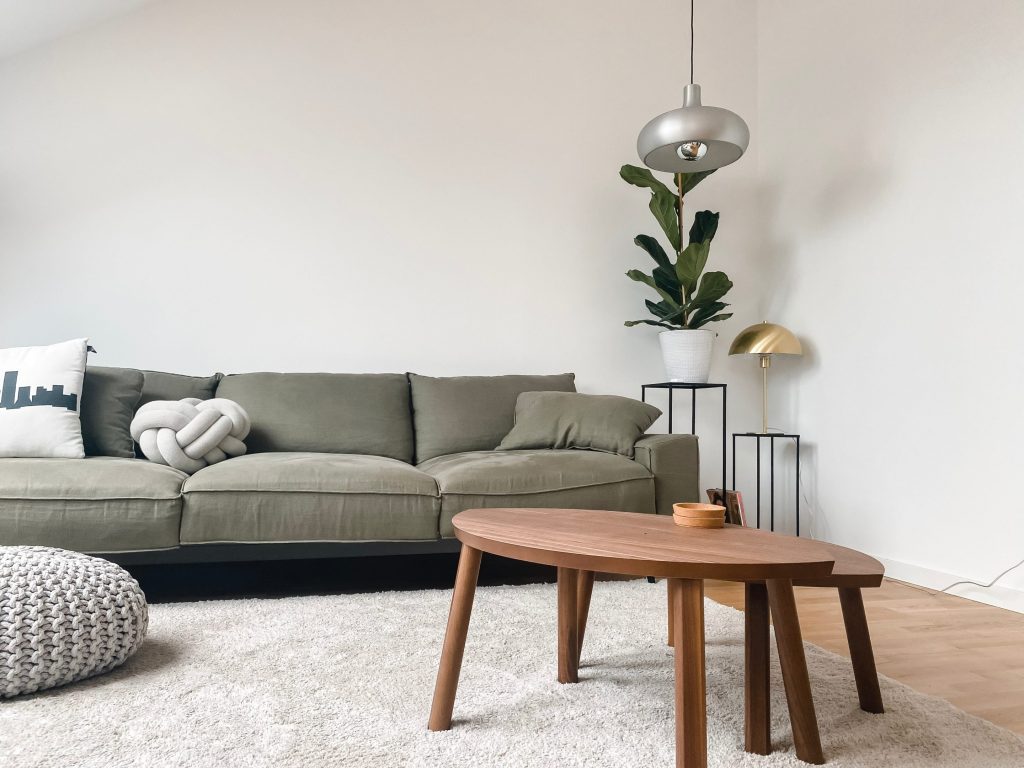 Modern living room with green sofa, wooden coffee table, and mixed metal accents including a silver pendant light and gold table lamp.