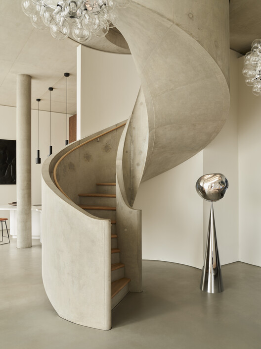 A modern interior featuring a sculptural concrete spiral staircase with a polished metal floor lamp. The design blends minimalism with artistic architectural elements, creating a unique residential space.