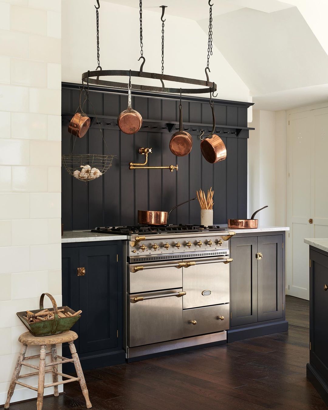 Elegant kitchen with a black and brass range, brass pot filler, and hanging copper pots, showcasing a mix of warm metals against dark cabinetry for a classic, refined look.