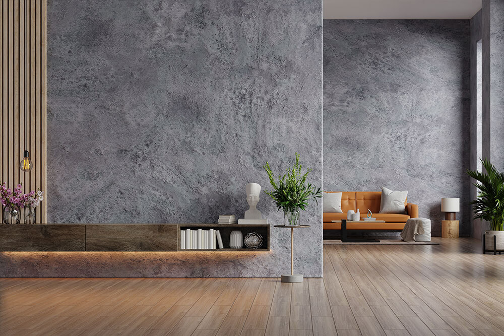 A modern living room featuring a beautifully textured gray wall with a natural finish, complemented by wooden slats, green plants, and a cozy orange sofa in a minimalist interior design.