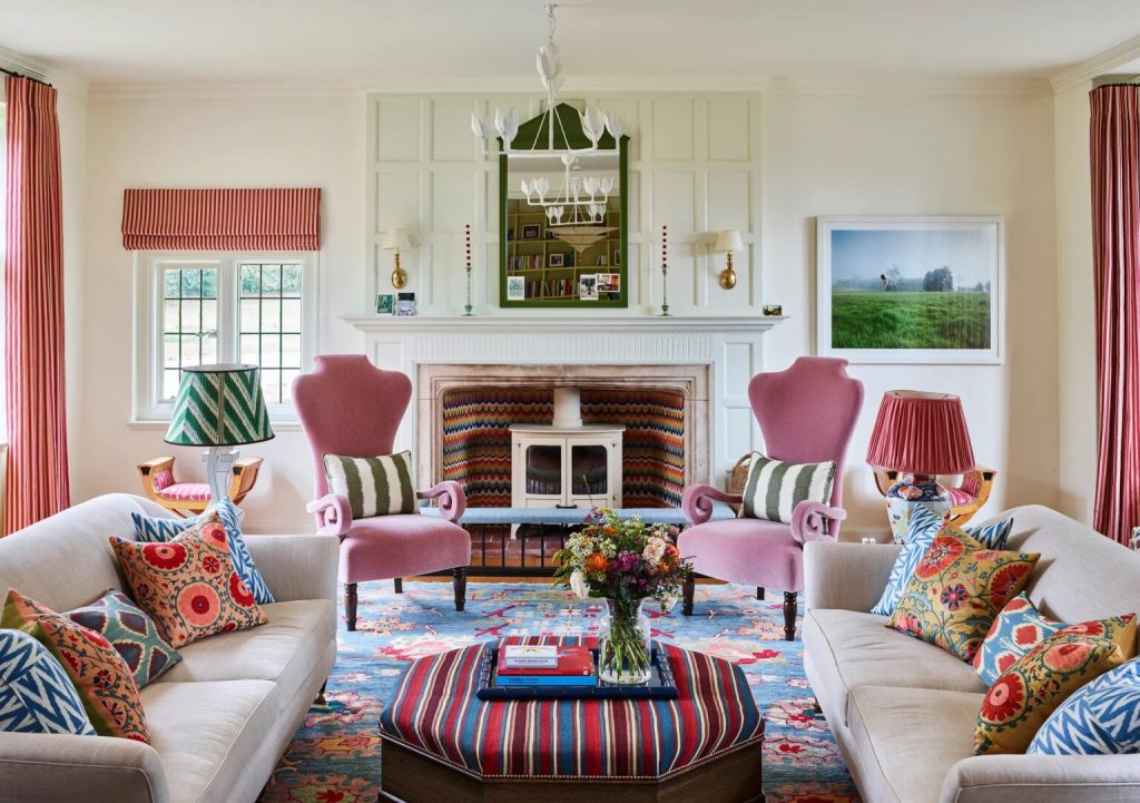 A vibrant living room with bold patterned cushions, a colorful rug, striped curtains, and pink accent chairs creating a lively and balanced mix of patterns and textures.