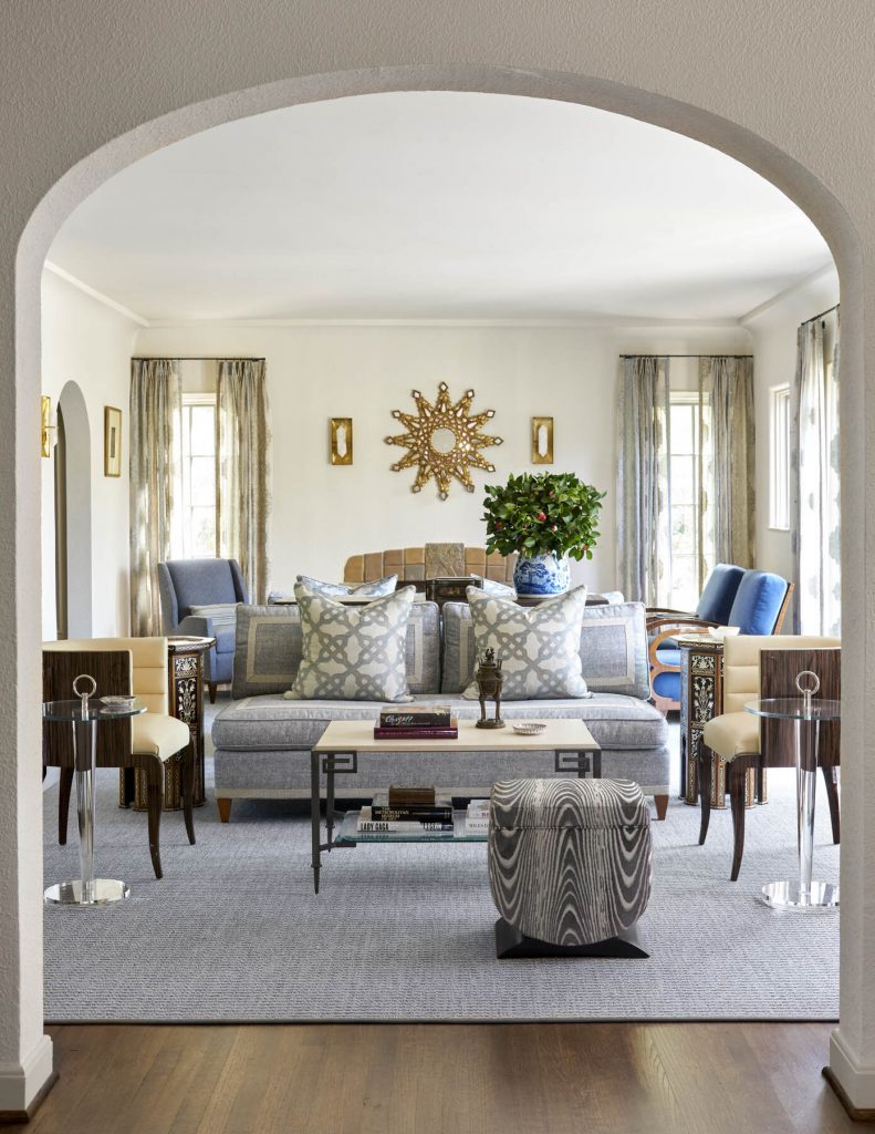 A sophisticated living room featuring a neutral-toned area rug, a patterned sofa with decorative pillows, accent chairs, and a stylish sunburst mirror, creating a balanced and inviting design.