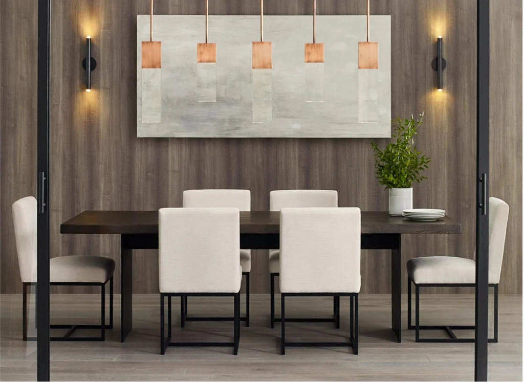 A modern dining room featuring a sleek dark wood table surrounded by six beige upholstered chairs with black metal legs. The wall showcases a large abstract painting, flanked by contemporary sconces. Above the table hangs a striking pendant light with copper accents. 