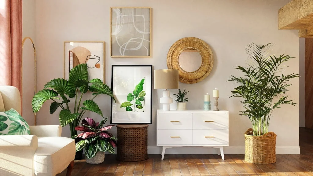 A cozy, nature-inspired interior corner featuring lush green plants, a white mid-century modern dresser with gold accents, and framed botanical artwork. A woven rattan mirror hangs above the dresser, complemented by candles, a table lamp, and decorative vases. The space is warmed by earthy tones, wooden flooring, and soft natural light filtering through pink curtains. A cream-colored armchair with a leaf-patterned throw pillow completes the inviting atmosphere. 